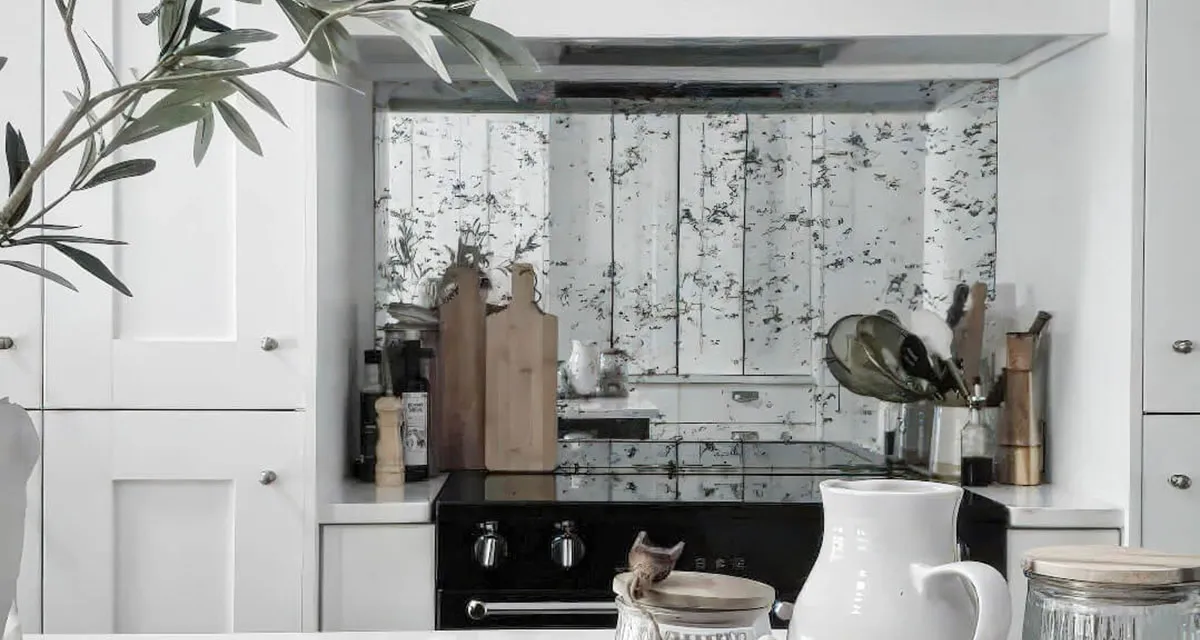 Antique mirror splashback fitted between the cooker hood and worktop in a white kitchen